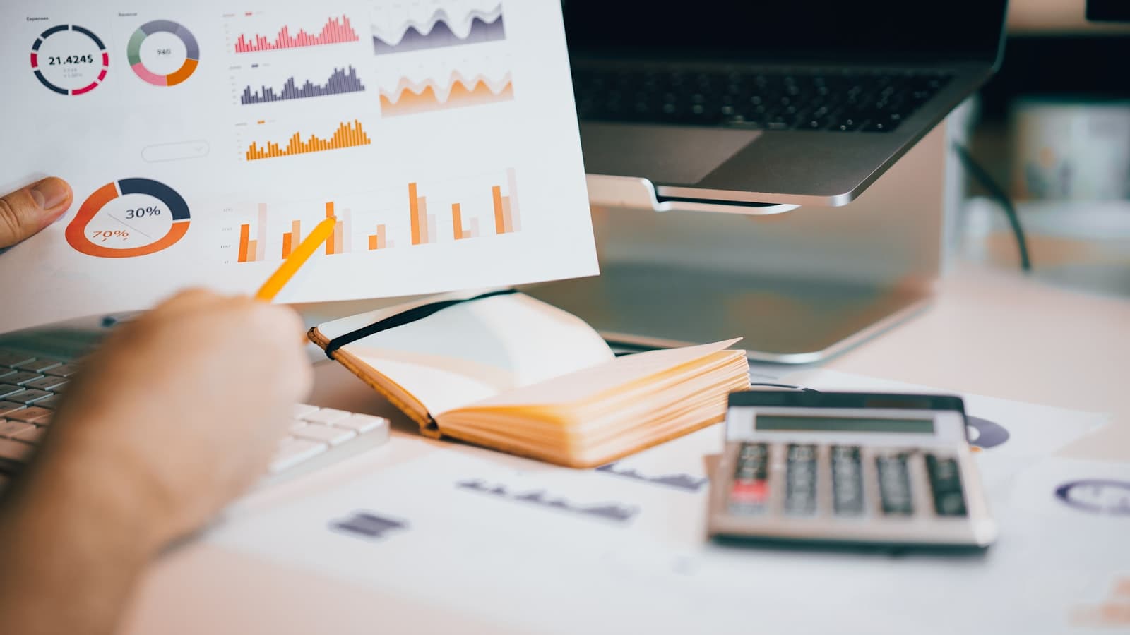 Agency owner reviewing a printed financial report with charts beside a laptop and calculator while calculating net profit margin