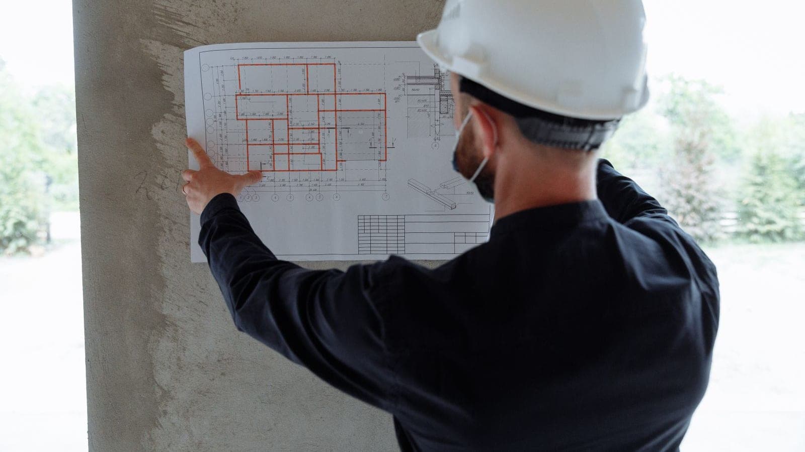 Architect in a hard hat checking a printed floor plan against the wall on an active construction site