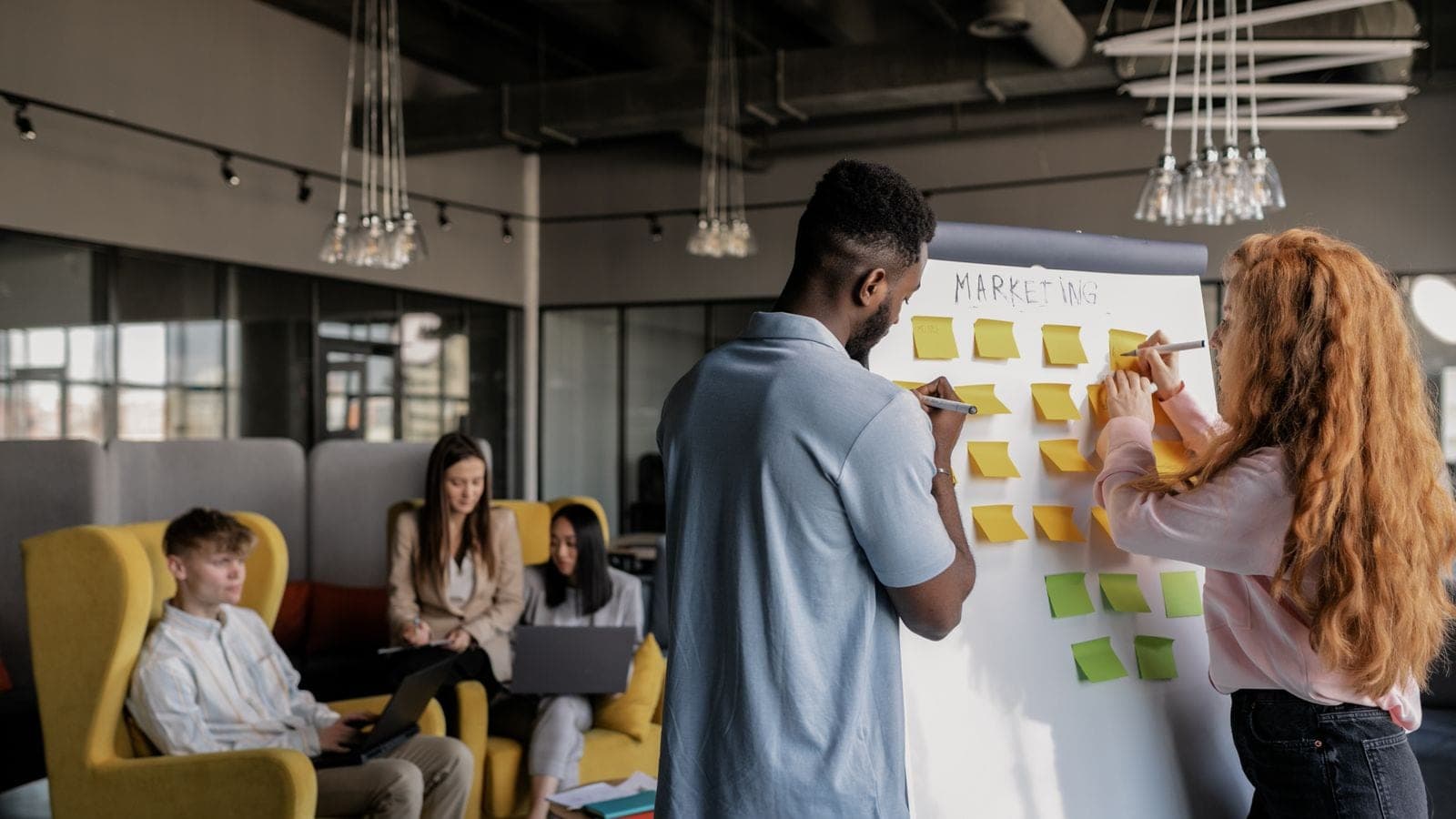 Marketing team planning a campaign with sticky notes on a whiteboard in an open office