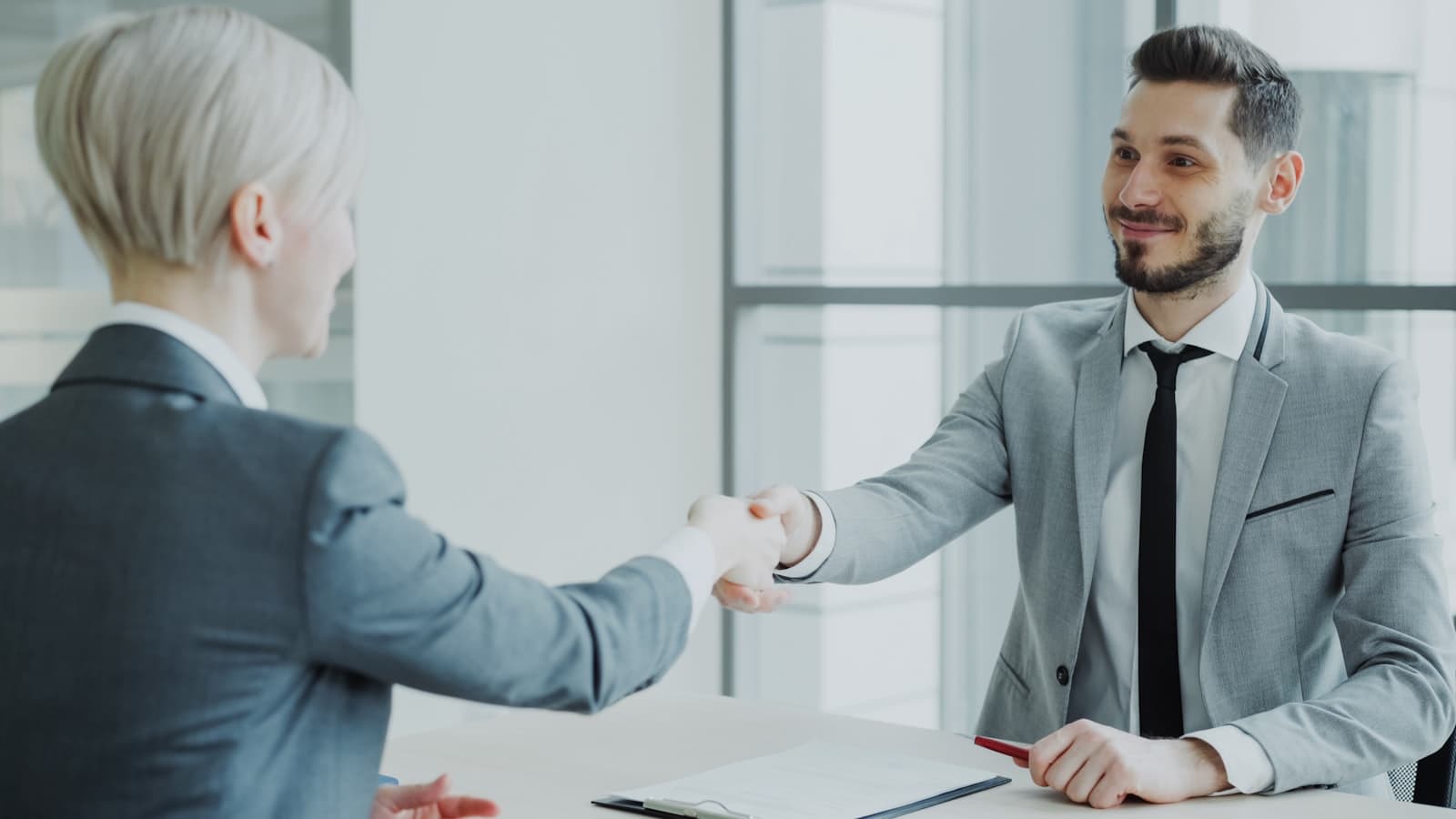 Agency lead and client shaking hands over a signed document at the close of a project engagement