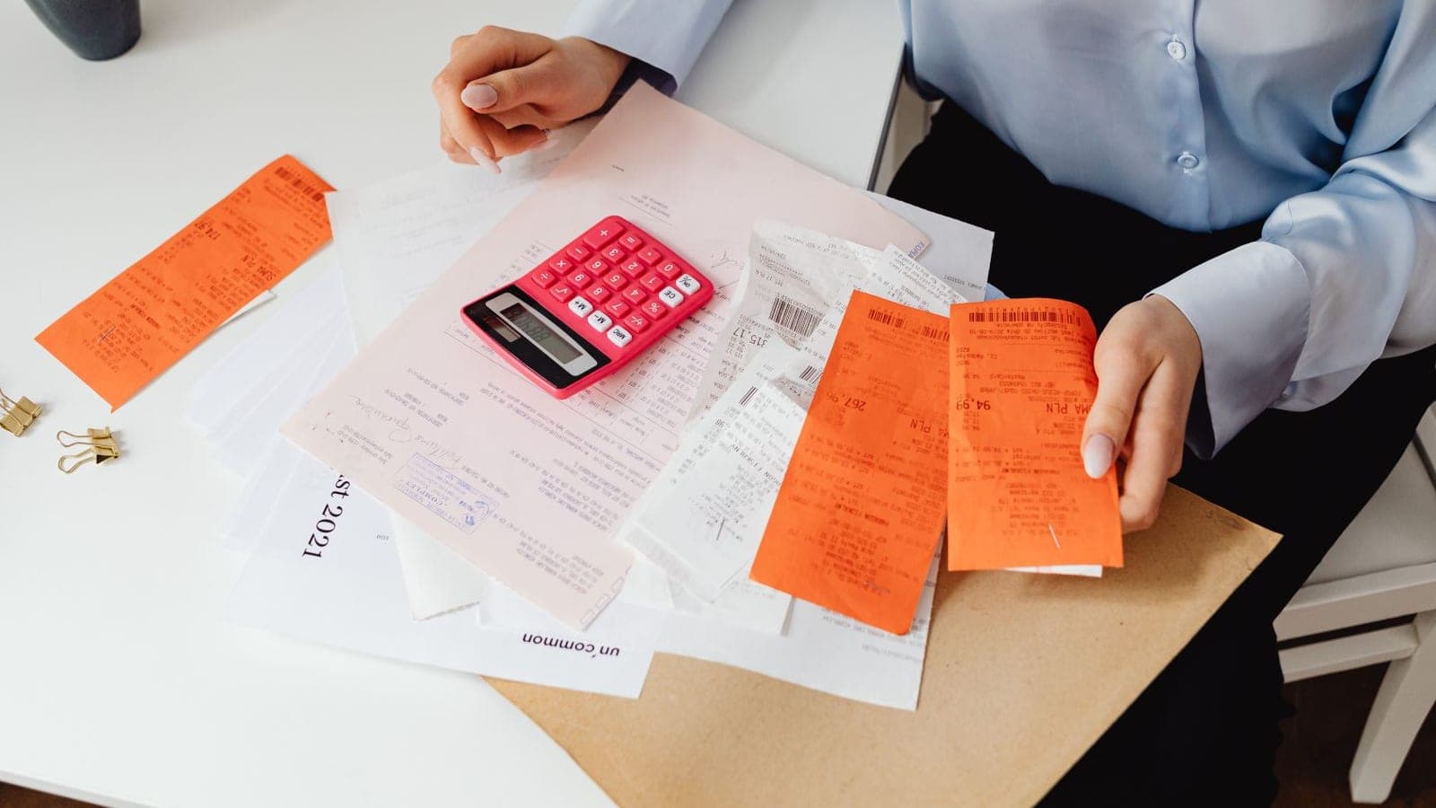 Hands sorting a pile of paper receipts next to a calculator on an agency desk