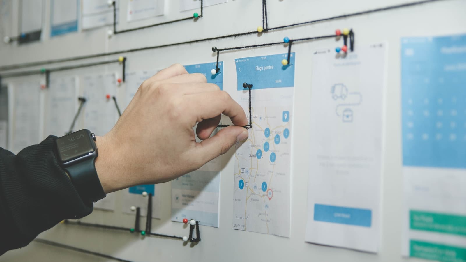 Person rearranging screens and cards pinned on a planning board, mapping columns before migrating projects to a new tool