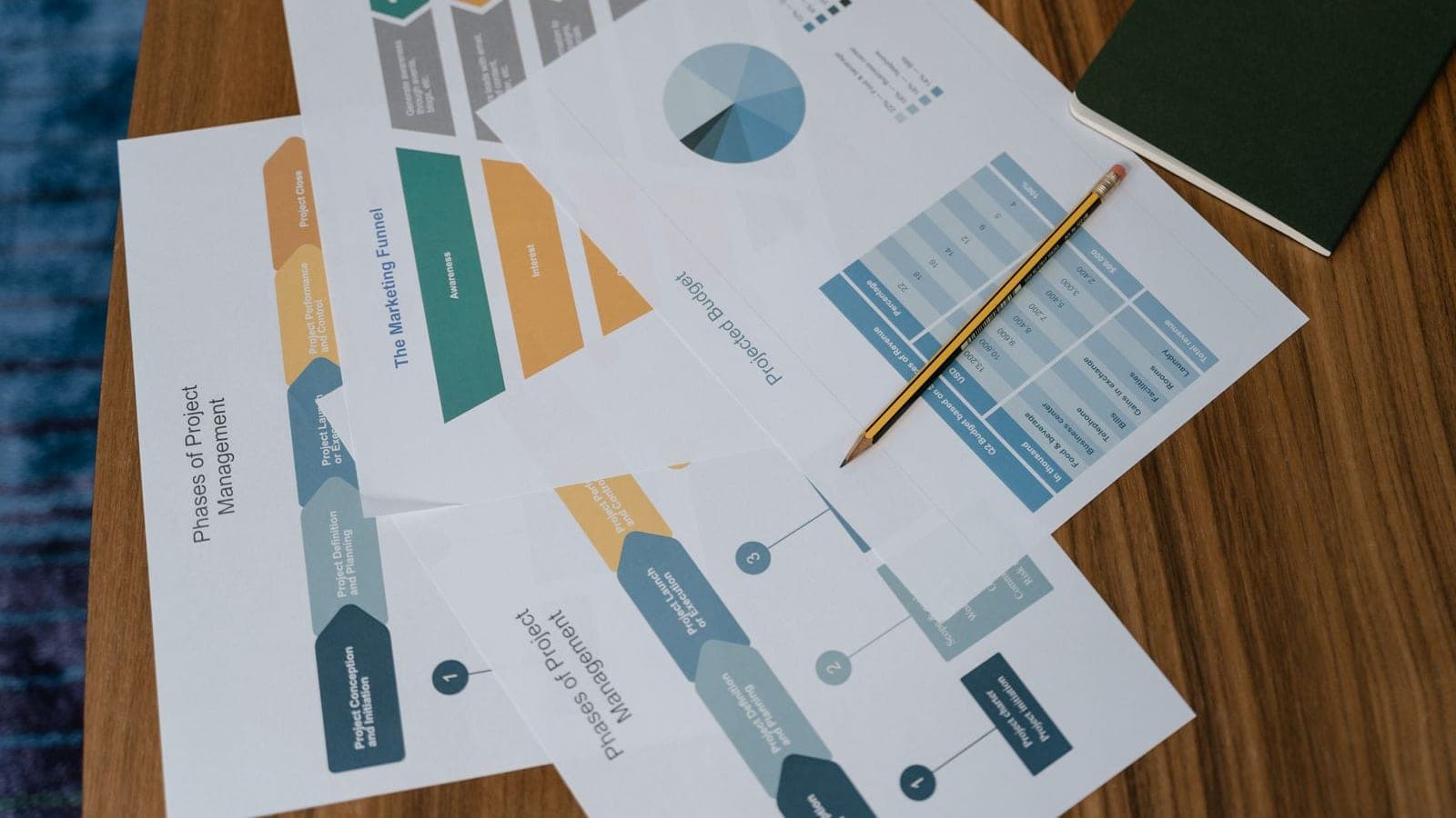 Printed project phase diagrams and schedule charts spread across a desk with a pencil
