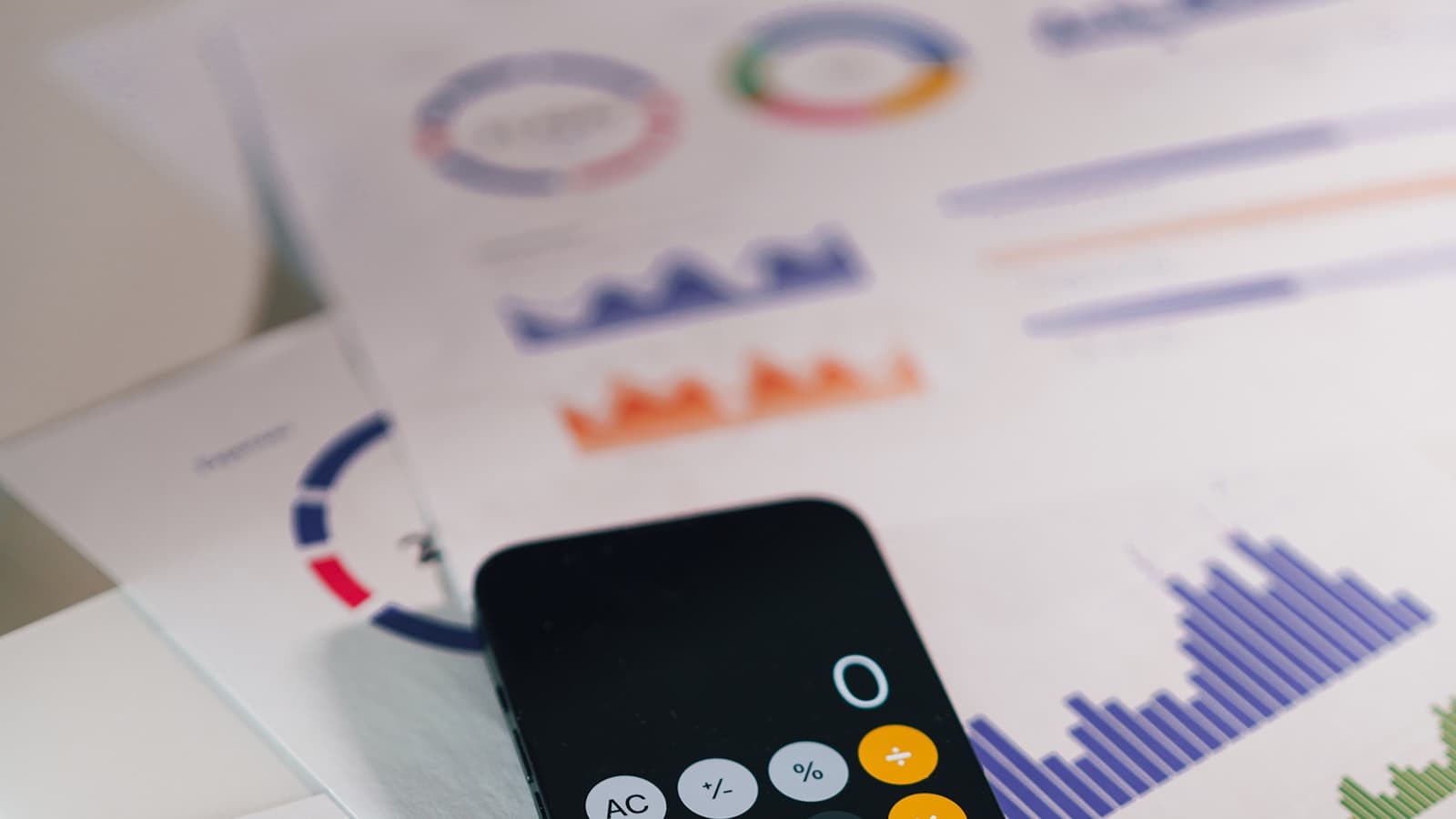 Calculator app on a phone resting on printed financial charts, used to compare an agency's billing rate against its realized hourly rate